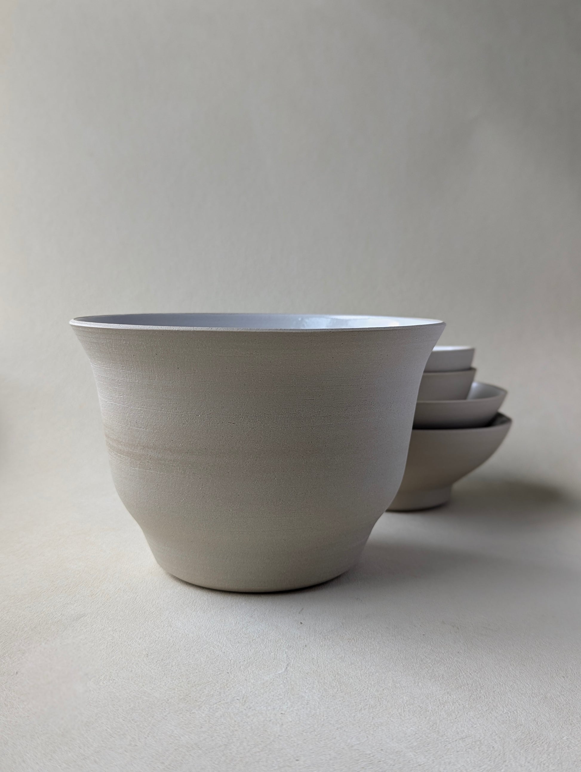 Side view of a big handmade stoneware salad bowl with a glossy white interior and raw exterior finish.