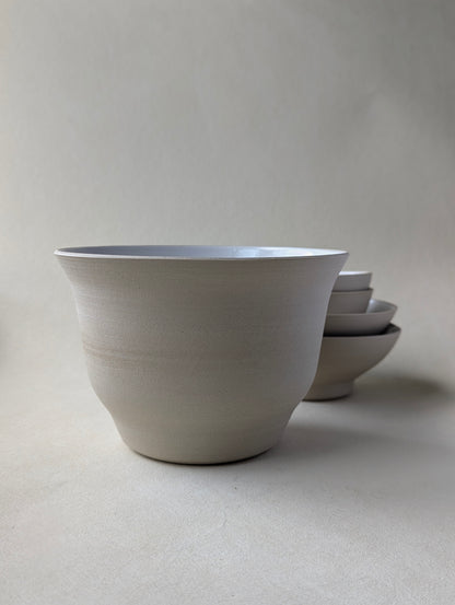 Side view of a big handmade stoneware salad bowl with a glossy white interior and raw exterior finish.