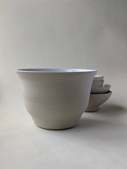 Side view of a big handmade stoneware salad bowl with a glossy white interior and raw exterior finish.