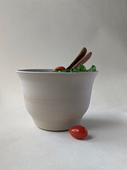 Handmade stoneware salad bowl with a glossy white interior and raw exterior, filled with fresh salad. Wooden salad spoon and fork are placed inside, showcasing the bowl’s elegant design and contrast finish.
