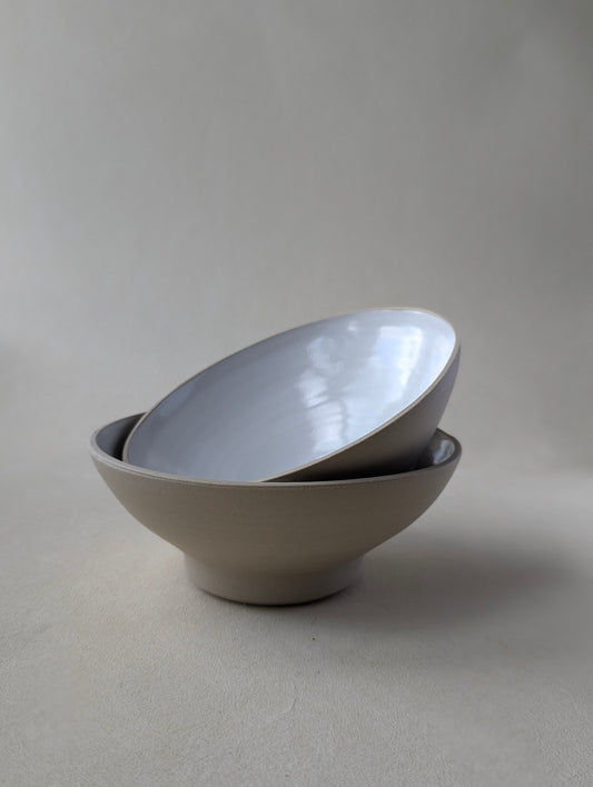 Two handmade stoneware snack bowls stacked, showcasing the glossy white interior and natural raw exterior.