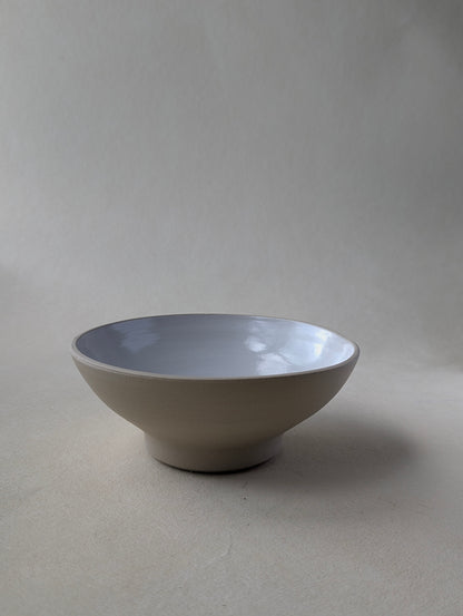 Side view of a handmade stoneware snack bowl with a glossy white interior and raw exterior finish.