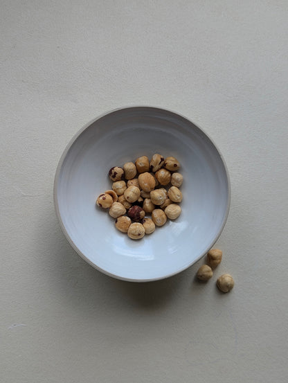 Handmade stoneware snack bowl filled with nuts, showing the glossy white interior and compact size.