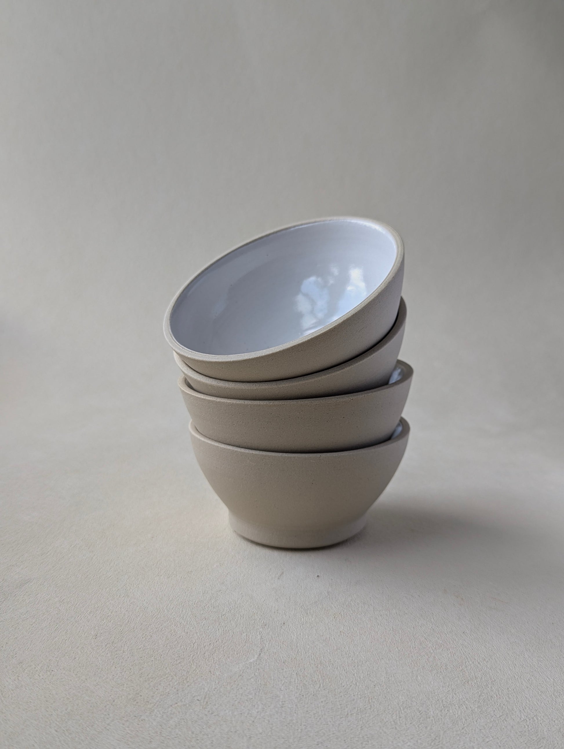 Four handmade stoneware snack bowls stacked, showcasing the glossy white interior and natural raw exterior.