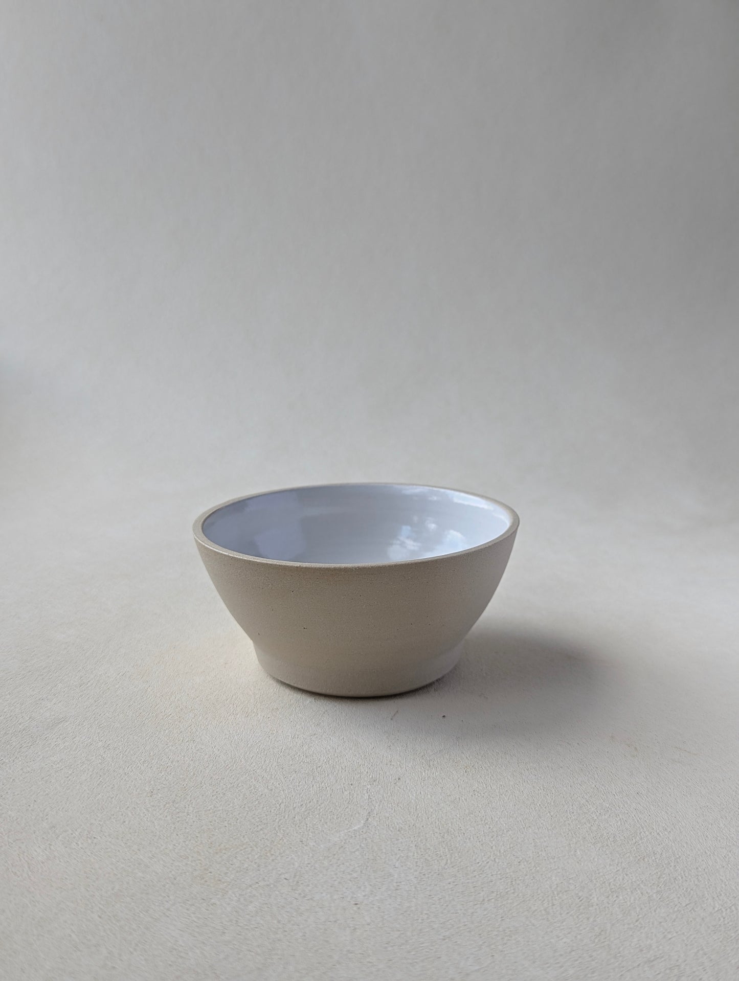 One handmade stoneware snack bowl, showcasing the glossy white interior and natural raw exterior.