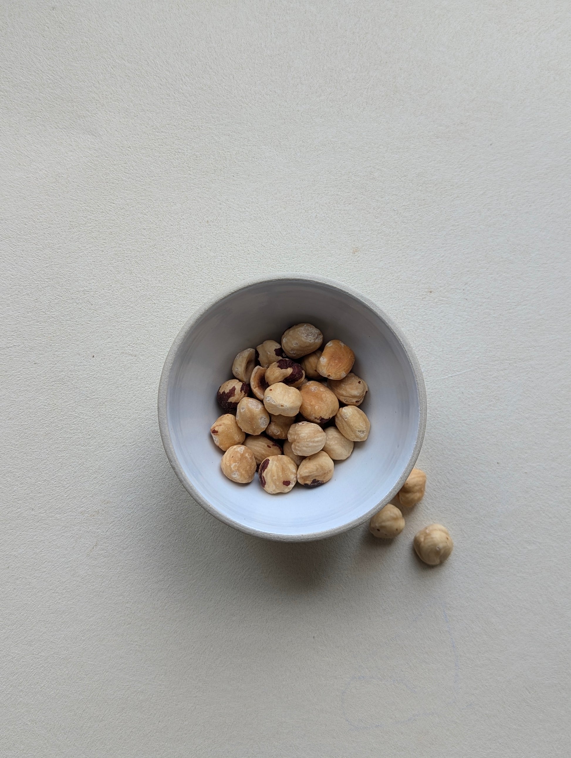 Handmade stoneware snack bowl filled with nuts, showing the glossy white interior and compact size.