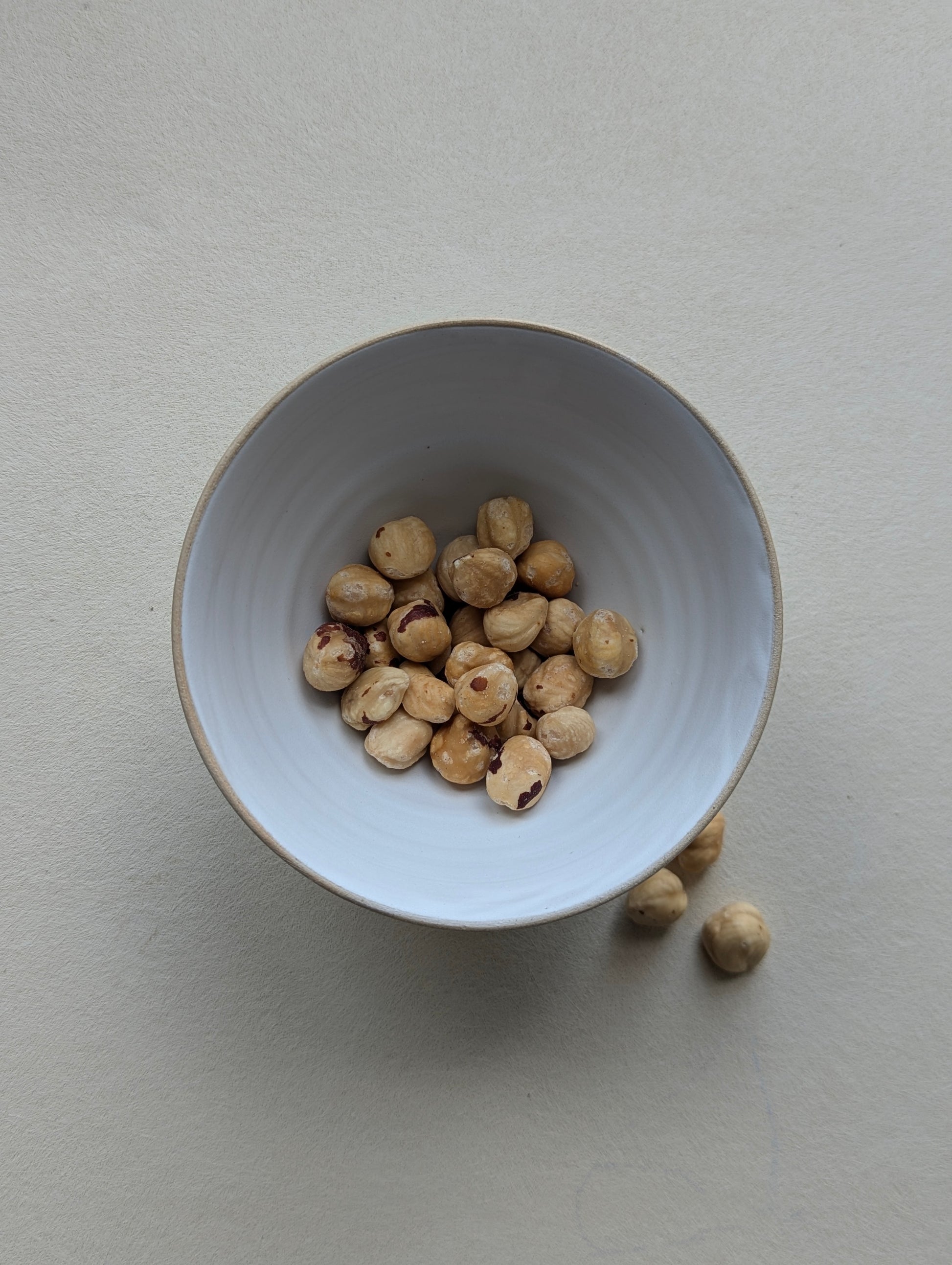 Handmade stoneware snack bowl filled with nuts, showing the matte white interior and compact size.